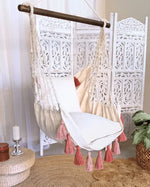 The Junior Hammock Chair Swing with Pink Tassels hangs in a living room.