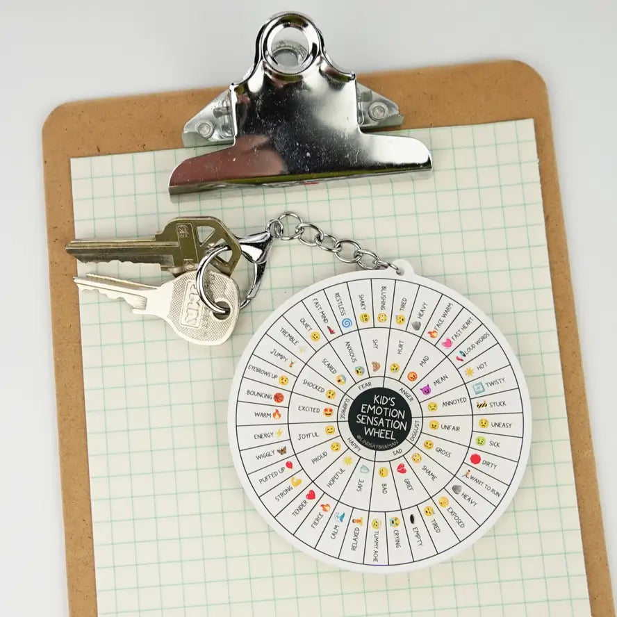 The Kid's Emotion Sensation Wheel Keychain with two keys, on top of a clipboard.