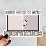 A hand holds a sticker that reads: I Love Someone With Neurotypicalness.