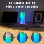 The Magic LED Cube Desk Lamp sits in a purple to green ombre on a counter top next to a laptop and a piece of art in a frame.