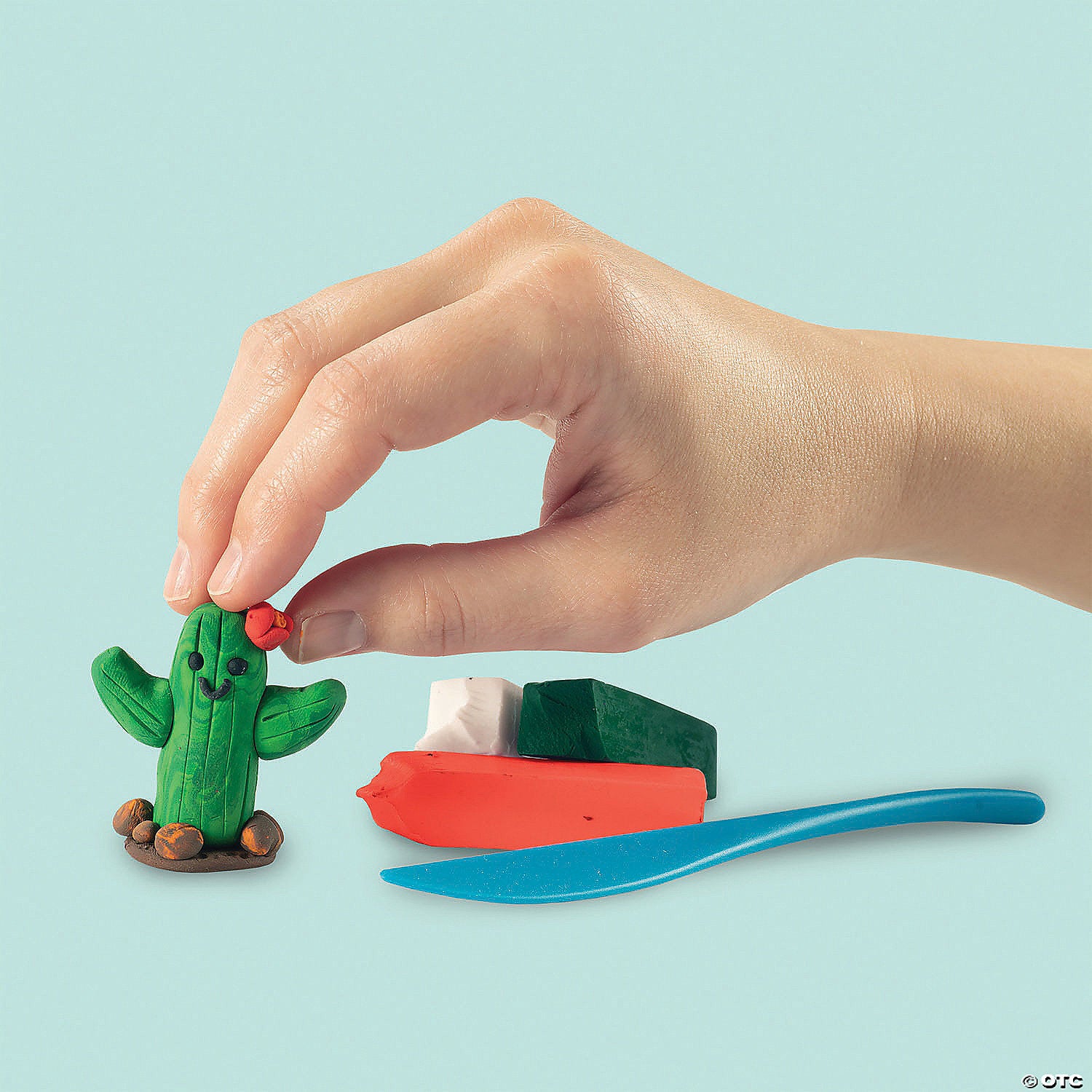 A hand with light skin tone touches the top of a cactus sculpted from the clay that comes with the MYO Light Up Snow Globes kit.