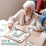 A woman sits at a table and plays with the Match the Dots Dominoes game.