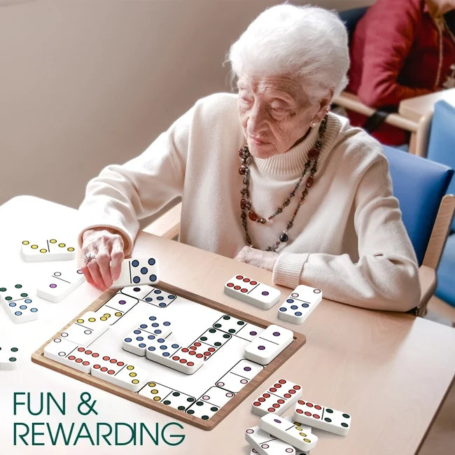 A woman sits at a table and plays with the Match the Dots Dominoes game.