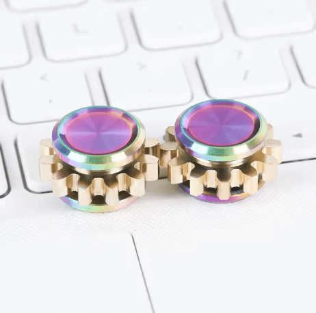 Two oil slick Mini Cog Fidgets next to each other on a keyboard.