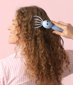 Someone pulls the light blue Modern Monkey Shrimp Scalpi Head Massager through their long brown hair.