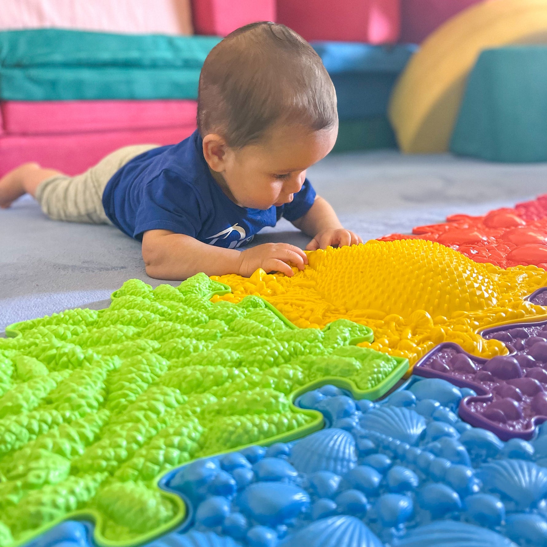 A toddler looks at the yellow Hedgehog mat while exploring it with its hands.