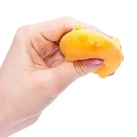 A hand squeezes the orange Teenie Nee Doh Cool Cat that has heart emoji eyes and is smiling.