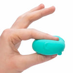 A hand squishes a teal Teenie Nee Doh Funky Pup, whose tail is facing the camera.