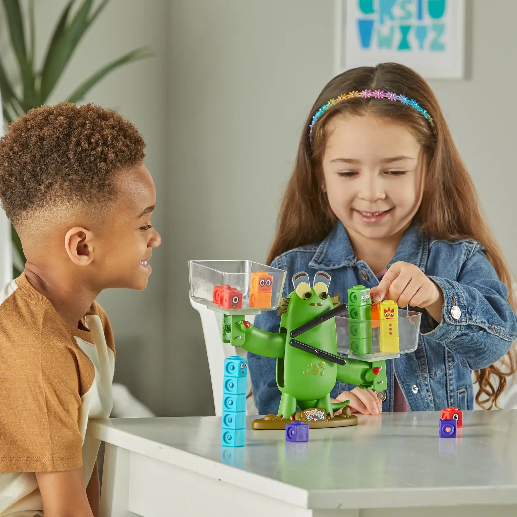 Two children sit at a table; one of them puts the number two into one of Blockzee's clear buckets.