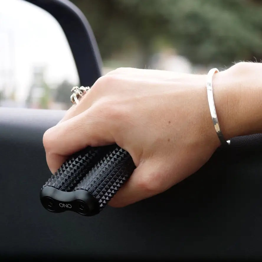 A hand holds the full size Ono Aluminum  Acupressure Roller and rests it on a car window sill. 