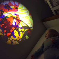 A baby looks up at the projection of a Liquid Wheel from the Aura Sensory Light Projector.