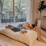 A woman and her dog lay on the white Pillow Lounger while it is in bed mode.
