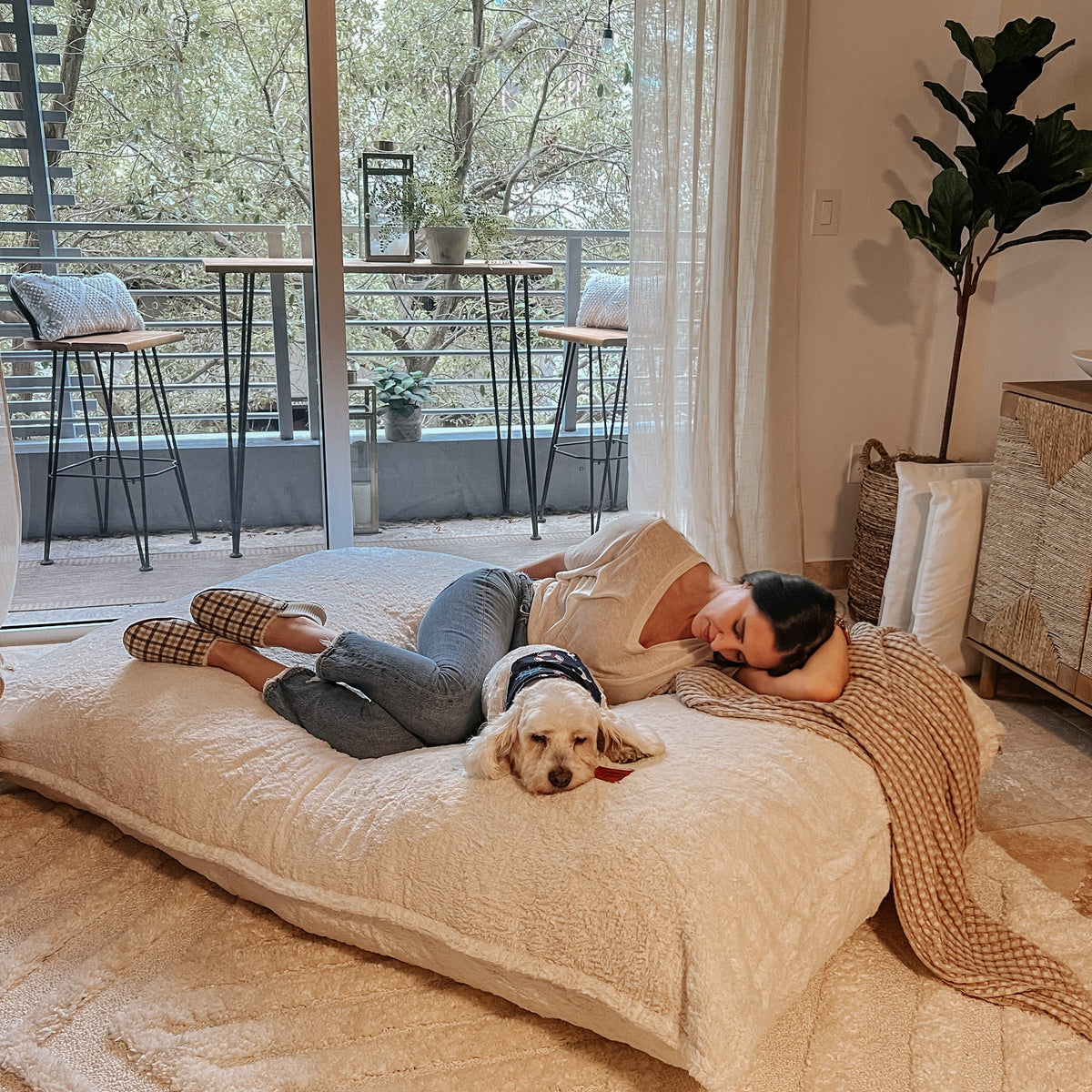 A woman and her dog lay on the white Pillow Lounger while it is in bed mode.