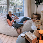 A woman drinks iced coffee while sitting on the white Pillow Lounger.