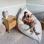 A woman reads a story to a toddler on the white Pillow Lounger.