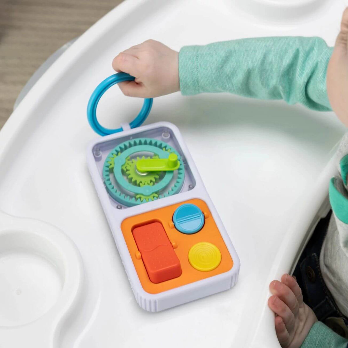 A toddler pulls the PlayTab Go Travel Sensory Activity Board by the ring across a tray.