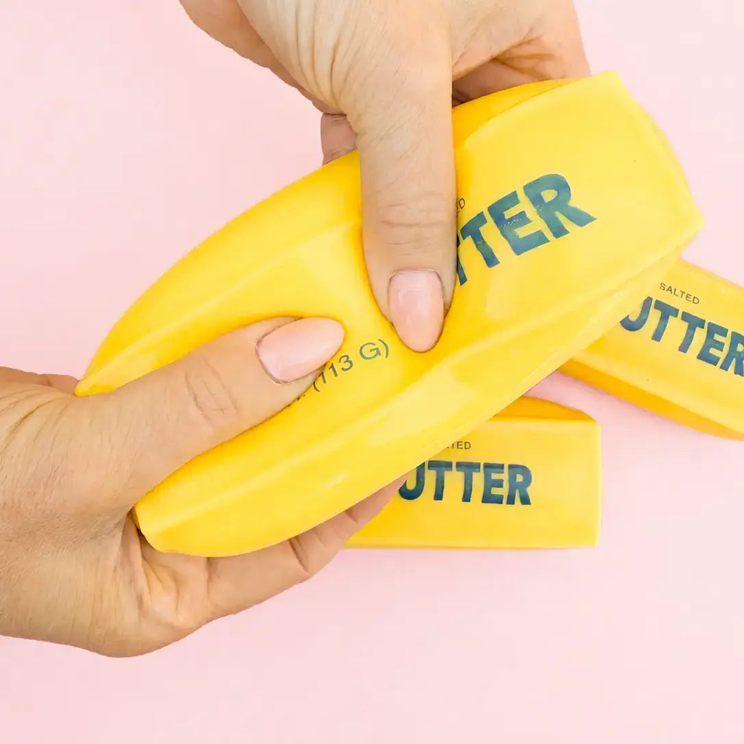 A hand squeezes either side of the Butter Me Up Slow Rise Squishy.