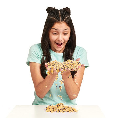 A person with medium-light skin tone and two french braids on the top of their head is holding up a large portion of Foam Alive Specklz and watching it run through their fingers.