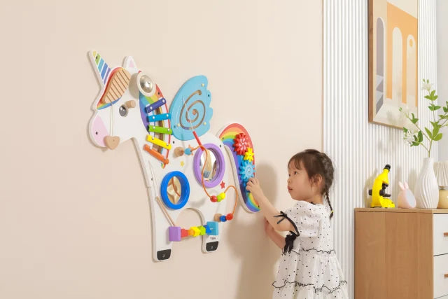 A child with light skin tone and brown braids plays with the cogs on the tail of the Unicorn Activity Wall Panels.
