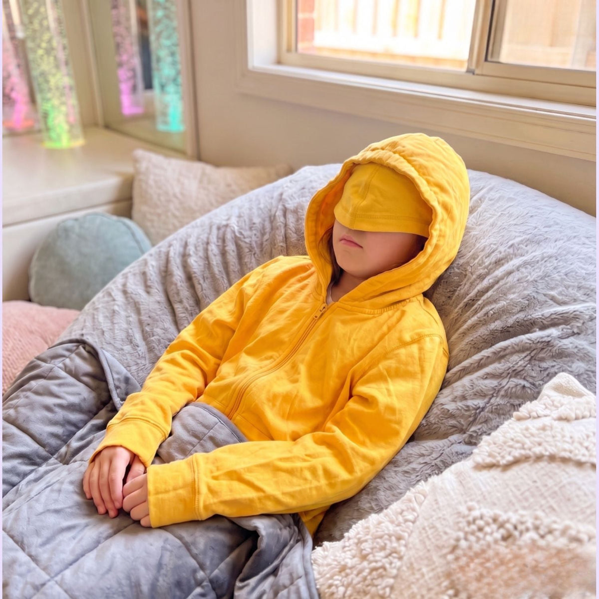 A child takes a nap with the eye mask over their eyes on their Kids QuietSense™ Zippered Sound Reducing Sensory Hoodie in Yellow.