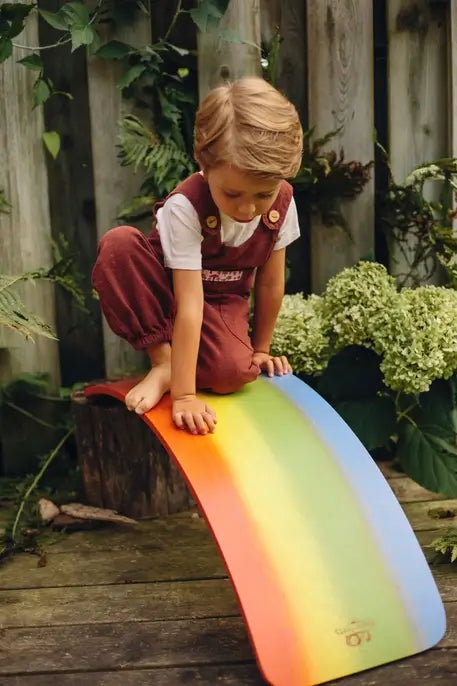 A child sits on top of the Kinderboard Rainbow Balance Boards.