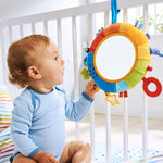 A baby sits in their crib and looks onto the HABA Rainbow Discovery Mirror while pulling on one of its effects.