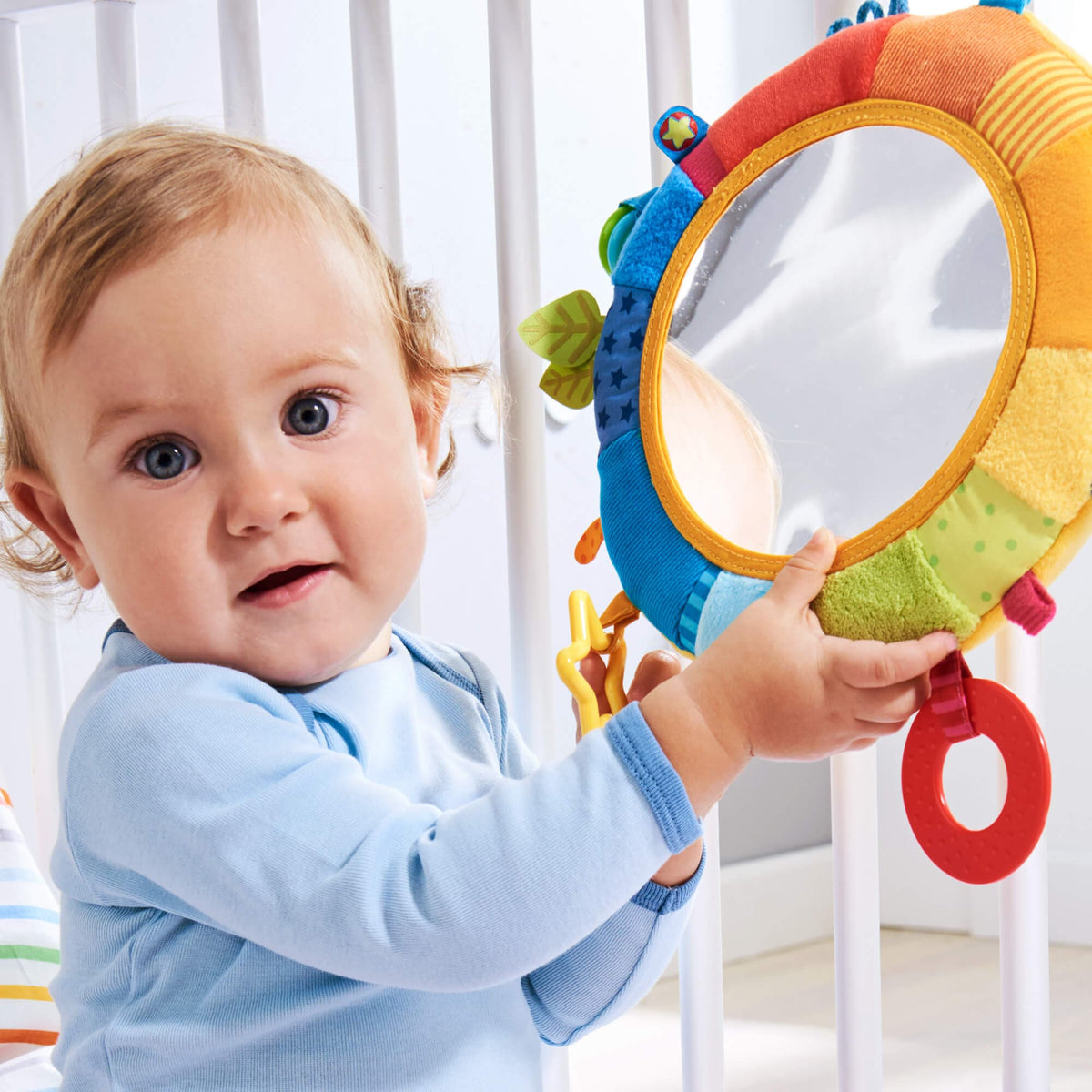 A child holds onto the Rainbow Discovery Mirror as it hangs off of their crib.