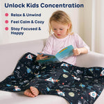 A child leans back on a couch and reads while covered by the Rocket Weighted Cooling Lap Pad 2 lb.