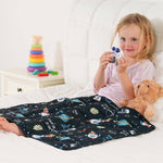 A child holds up two astronaut toys while laying in bed, covered by the Rocket Weighted Cooling Lap Pad 2 lb.