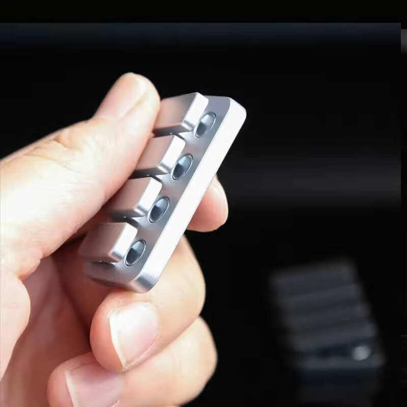 A hand holds the silver Magnetic Haptic Clicker Fidget.