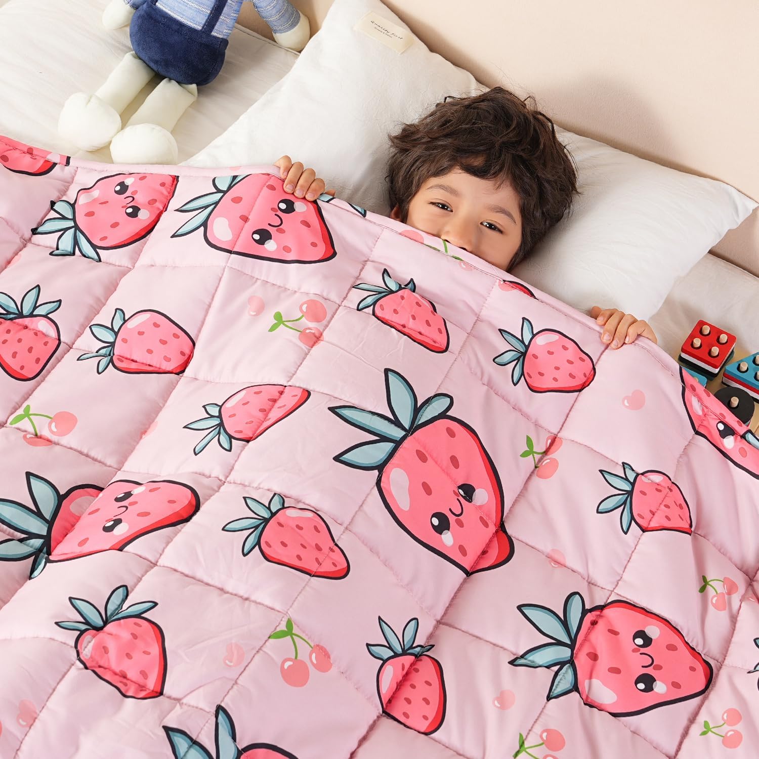 A child peeks out from underneath the 
Strawberry Washable Cooling Weighted Blanket for Kids - 5 lb.