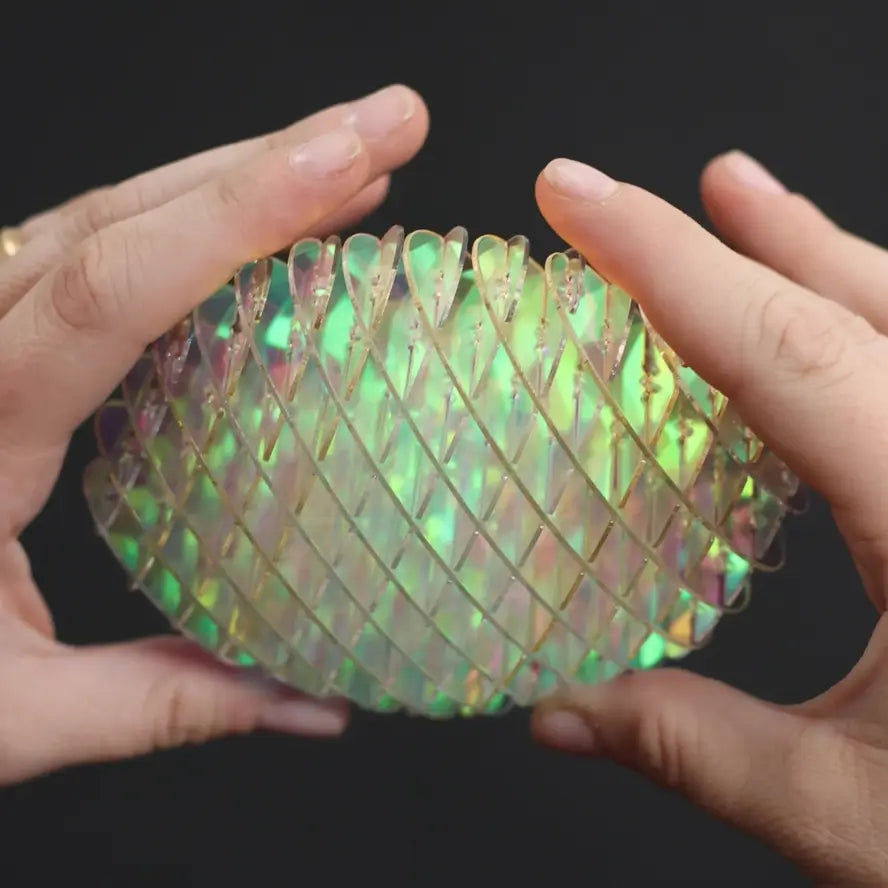 Two hands hold the Small Unicorn Fidget Worm to reflect the light.