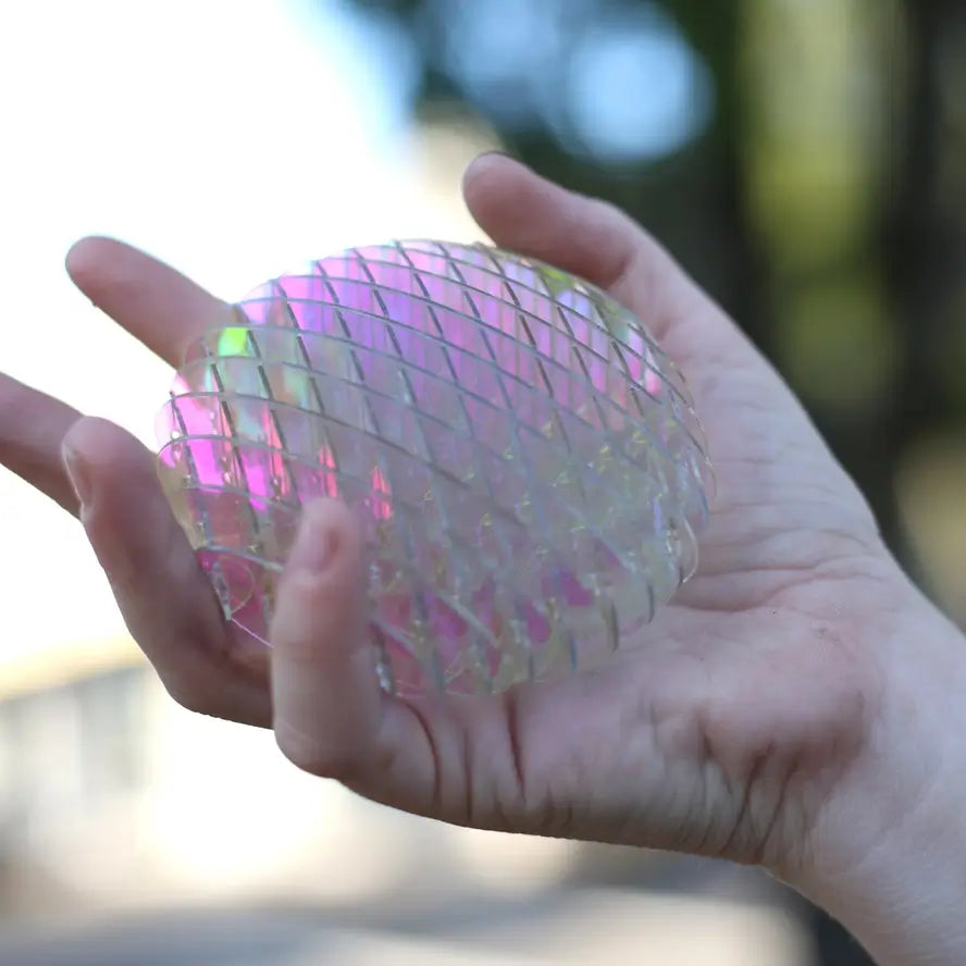 A hand holds up the Small Unicorn Morf Fidget Worm to reflect the natural light.