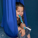 A child sits in a compression swing while chewing on the Spaghetti Chewy Fidget.