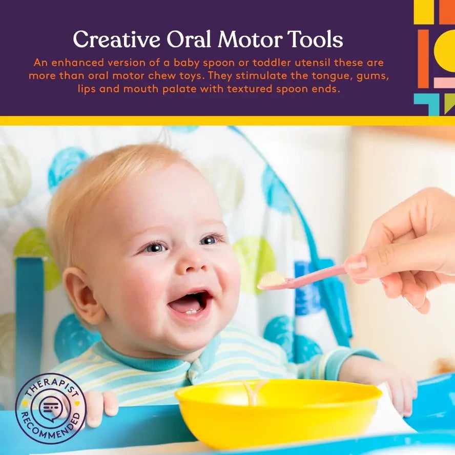 A hand extends a Light Pink Duo Spoon covered in applesauce to a smiling baby in a high chair.