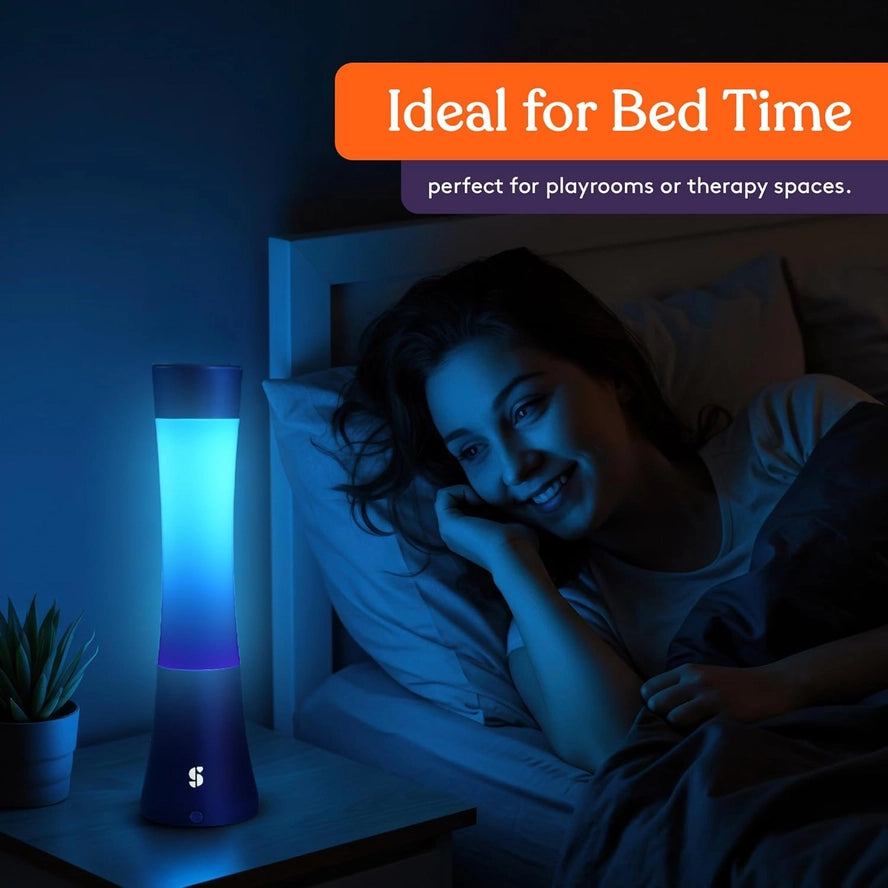 A woman looks at the ombre blue glow of the Light Lava Lamp on a bedside table.