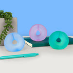 The three color variants of Speks Gump Loop Cool 3-Pack on a stylized background with a notebook.