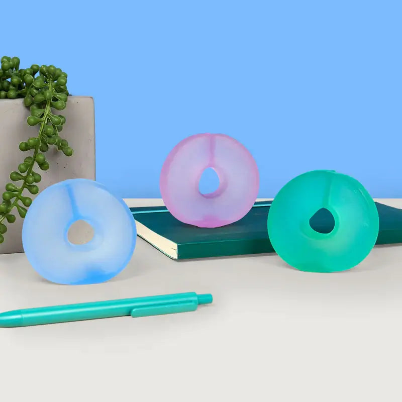The three color variants of Speks Gump Loop Cool 3-Pack on a stylized background with a notebook.