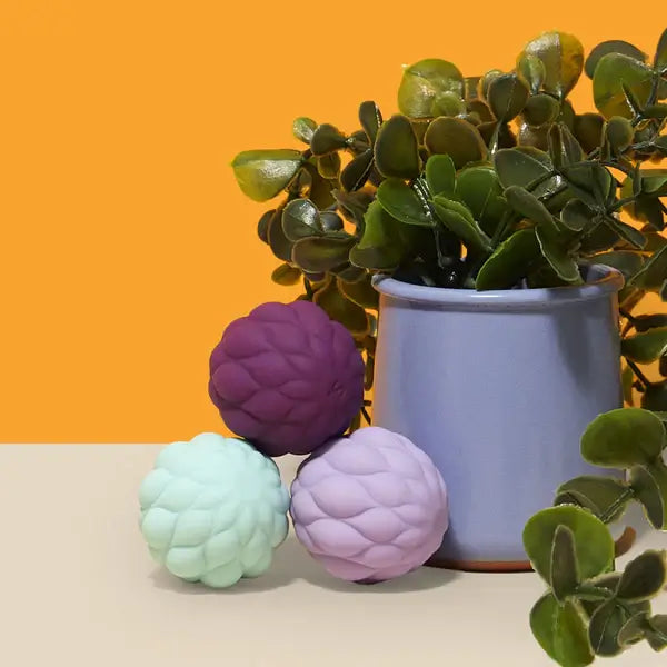 The Speks Odds Vivid Purple Puffs are stacked in front of a house plant.