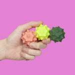 A hand holds the three Speks Odds Vivid Green Spurs against a pink background.
