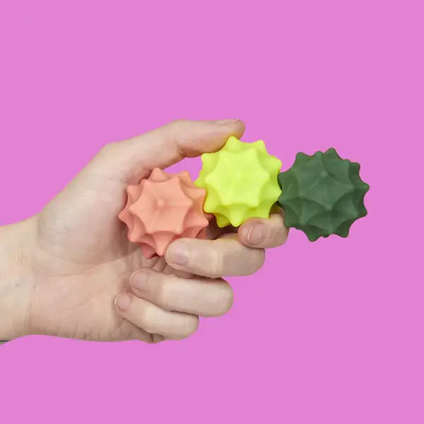 A hand holds the three Speks Odds Vivid Green Spurs against a pink background.
