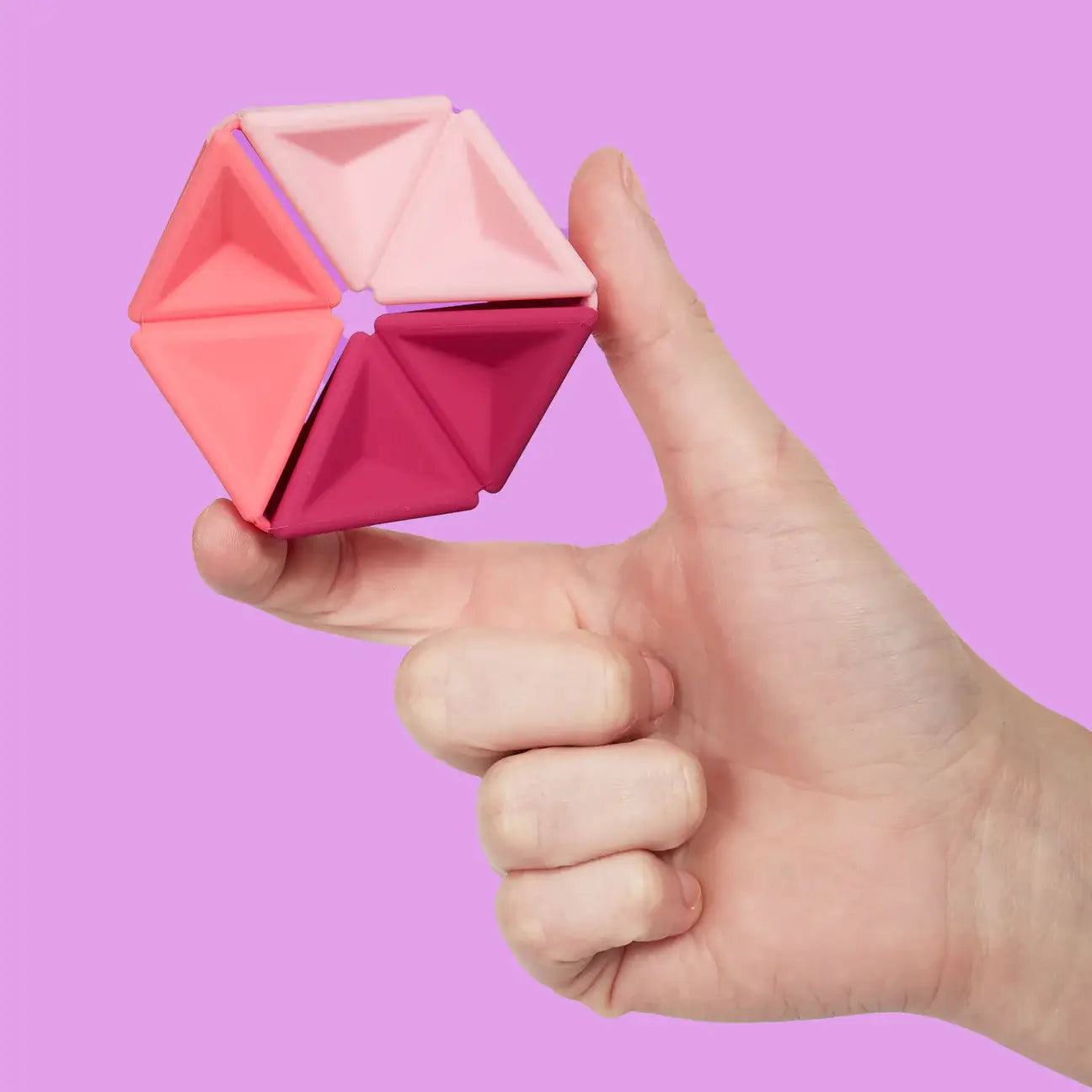 A hand holds the Speks Magenta Pivot Silicone Flexagon against a purple background.