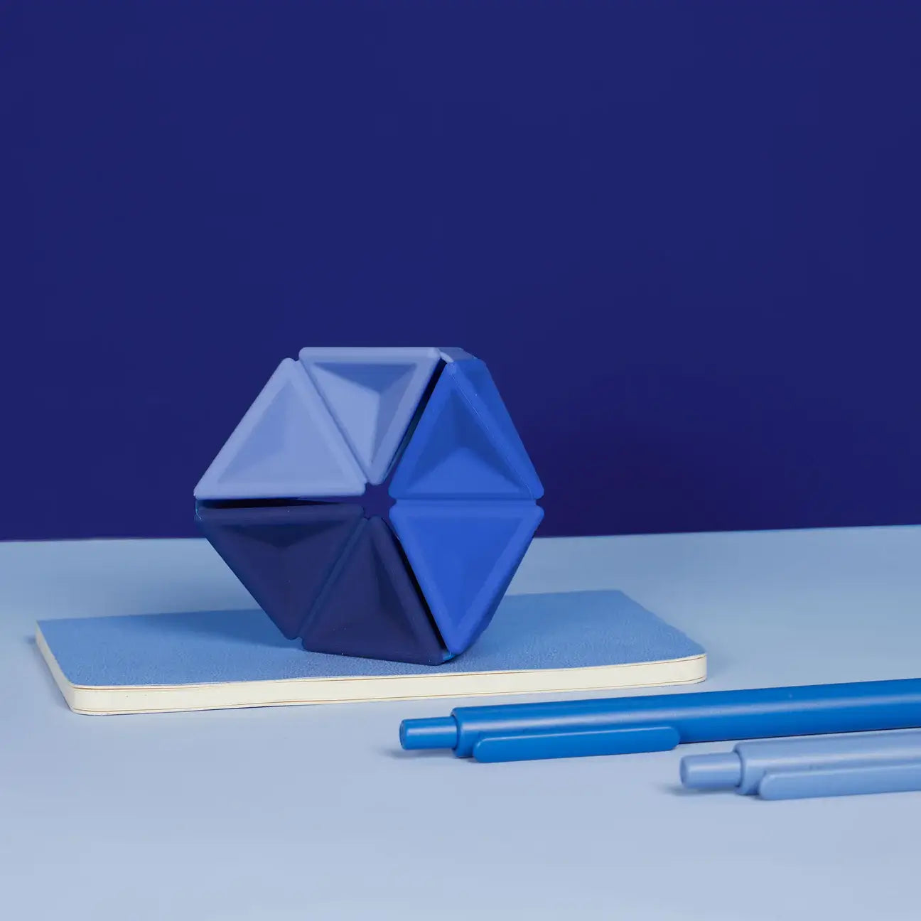 The Speks Navy Pivot Silicone Flexagon on top of a small blue notebook.