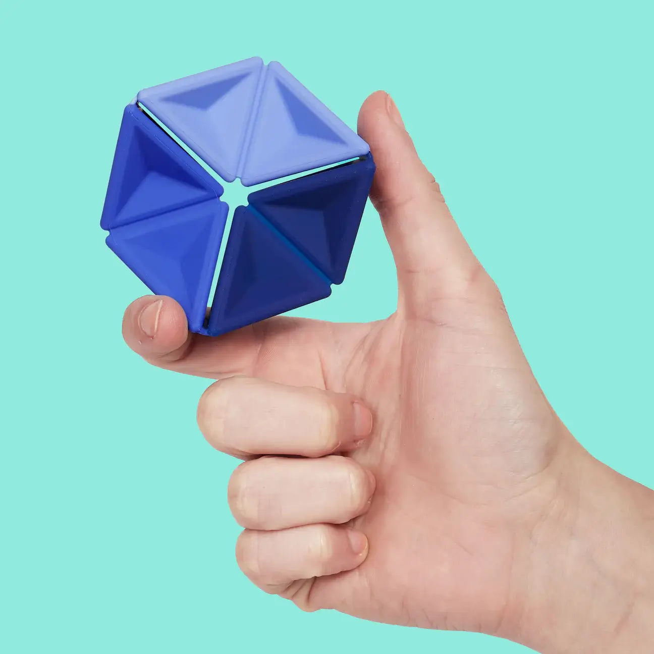 A hand holds up the Speks Navy Pivot Silicone Flexagon in front of a teal background.