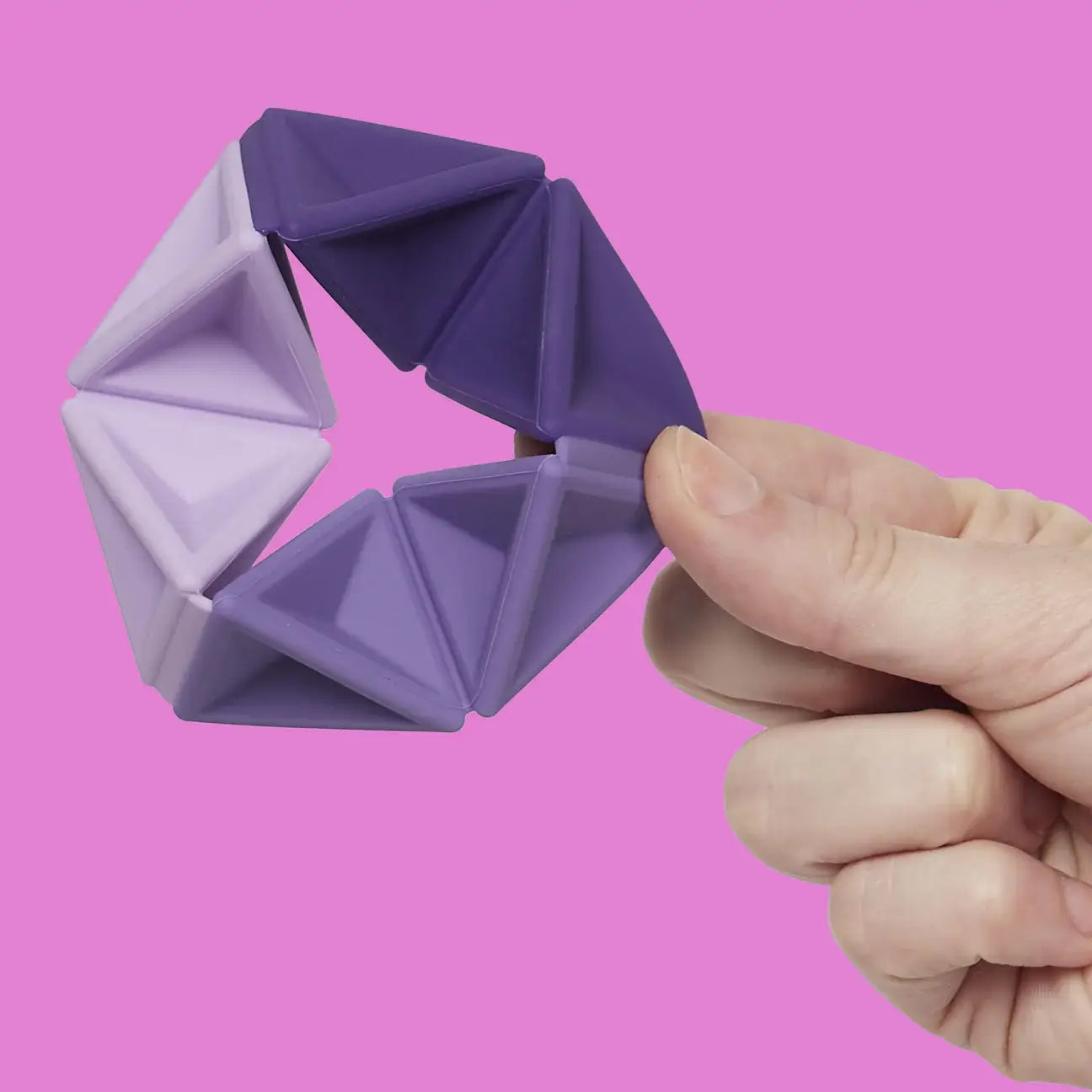 The Speks Violet Pivot Silicone Flexagon being held by a hand in front of a pink background.