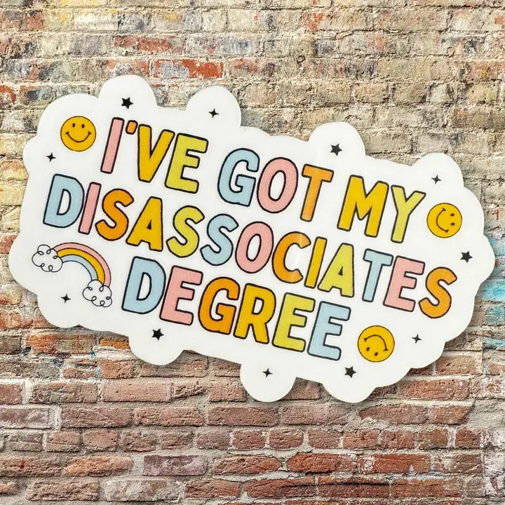 The rainbow colored I've Got My Disassociates Degree Vinyl Sticker on a brick background.