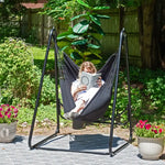 Someone lounges with their legs curled up on a patio in the Polycotton Hammock Chair A-Frame Steel Stand.