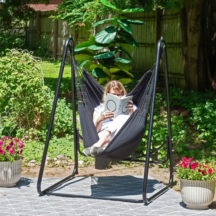 Someone lounges with their legs curled up on a patio in the Polycotton Hammock Chair A-Frame Steel Stand.