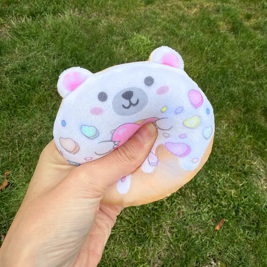 A hand gently squeezes the white Super Duper Sugar Squisher Sugar Bear Donut.