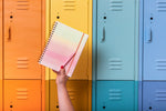 A hand holds up the Daybreak Undated Perpetual Planner in front of colorful lockers.